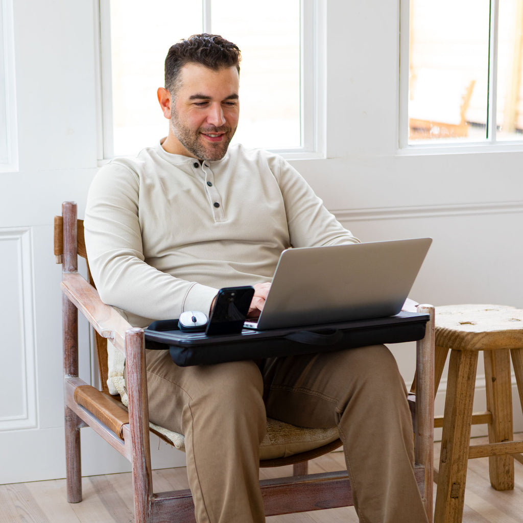 Lifestyle image of a man using a lap desk while sitting in a chair.