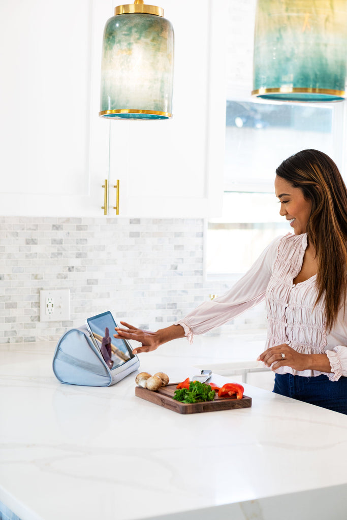 Woman cutting vegetables in the kitchen while looking at a recipe on her tablet that is sitting in the Tablet Pillow Stand.