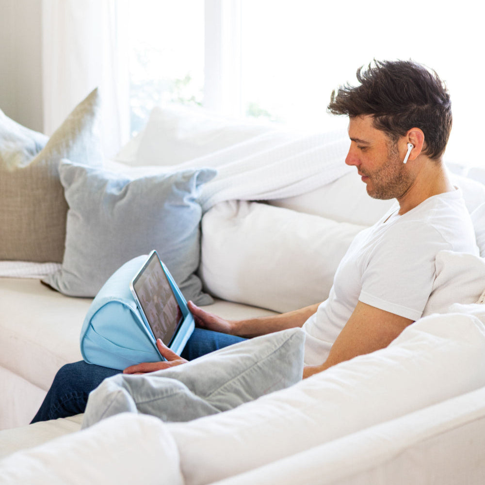 Sky Blue Tablet Pillow Stand Lifestyle of a man using his tablet in the tablet pillow stand while sitting on the couch.