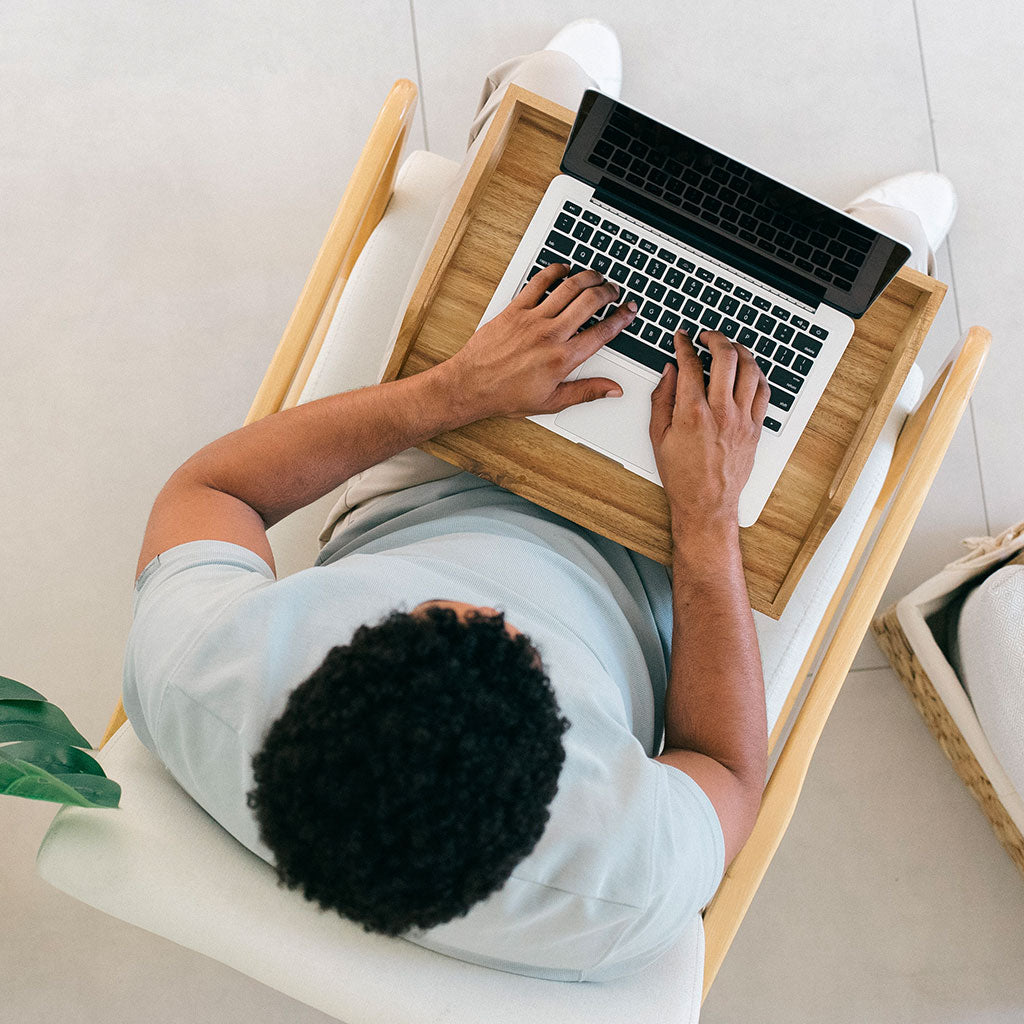 Person using a laptop on a wooden tray with a white background